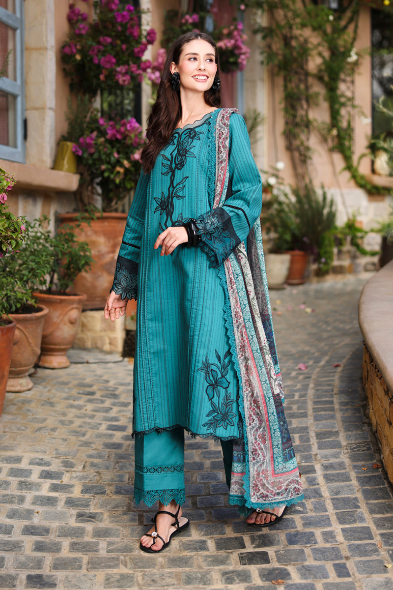 Woman in a teal embroidered outfit standing on a stone path with plants in the background