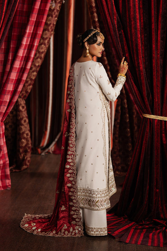 Woman in traditional white and gold outfit standing behind red curtains