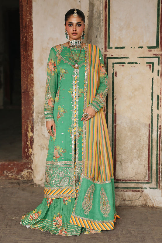 Woman in a green and yellow traditional outfit standing against an ornate wall.