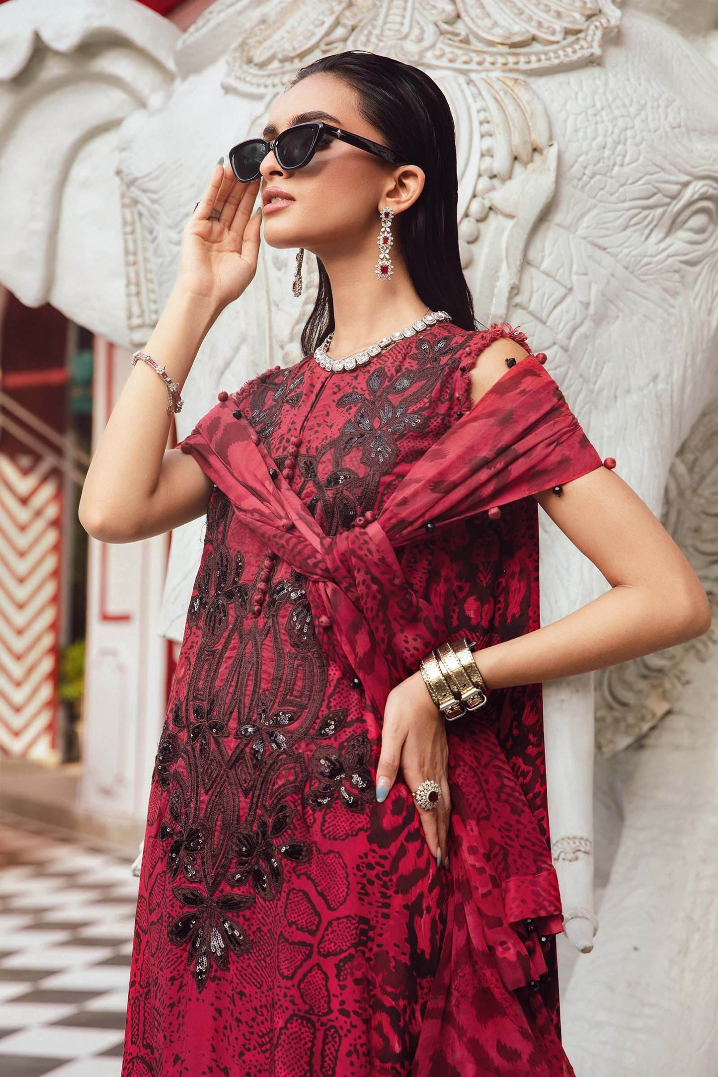 Woman in a red and black embroidered dress standing next to a white elephant statue.