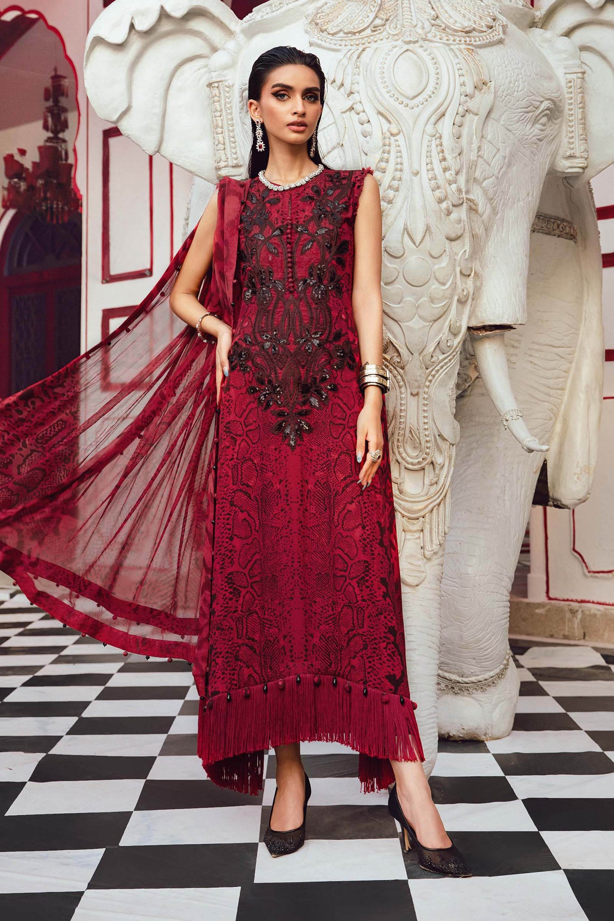 Woman in a red dress standing next to a large decorative elephant statue in an ornate room.