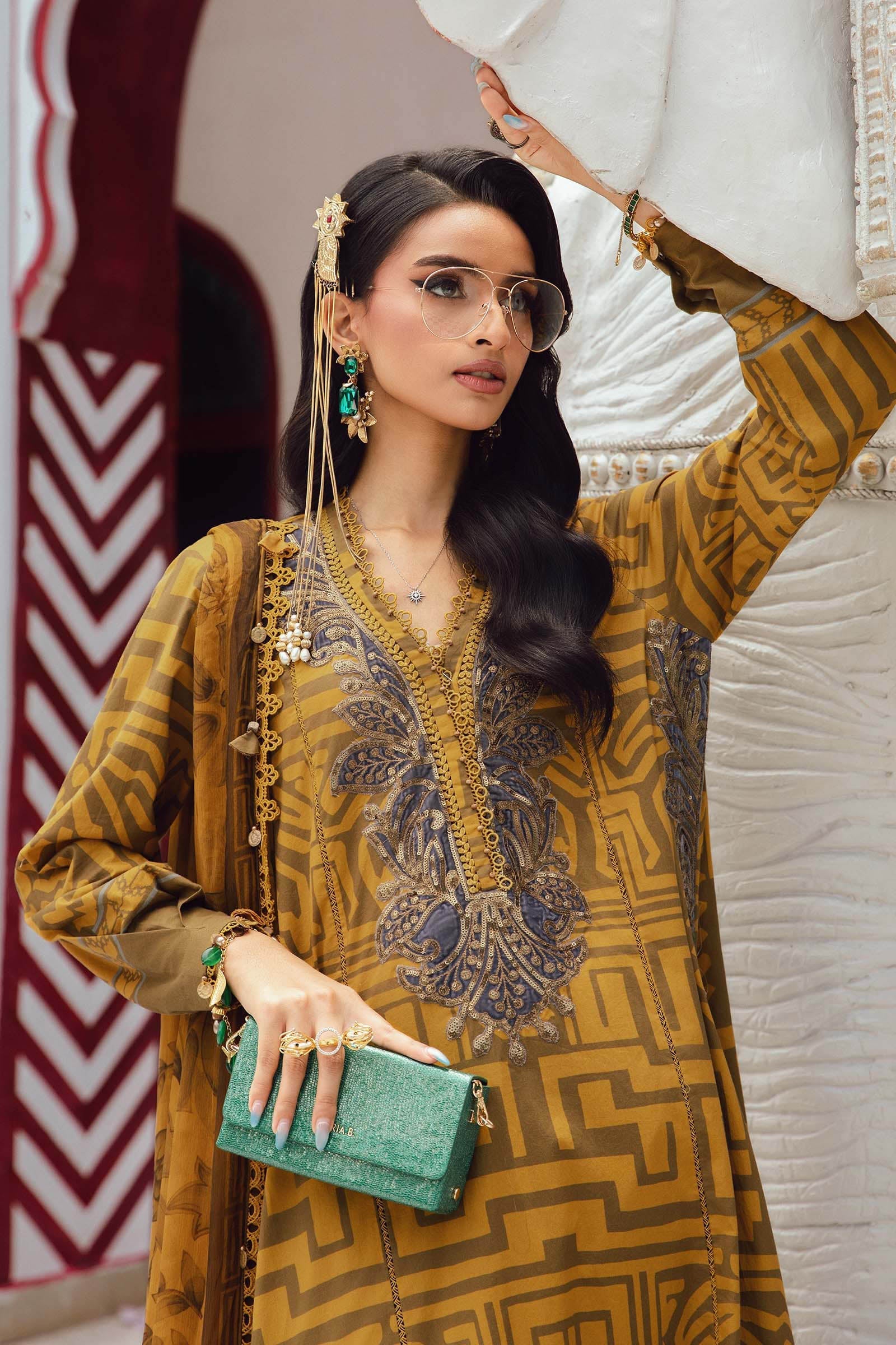 Woman in a patterned outfit holding a white garment against a decorative wall.