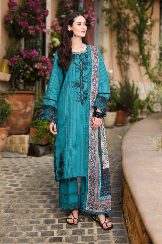 Woman in a teal embroidered outfit standing outdoors with plants in the background