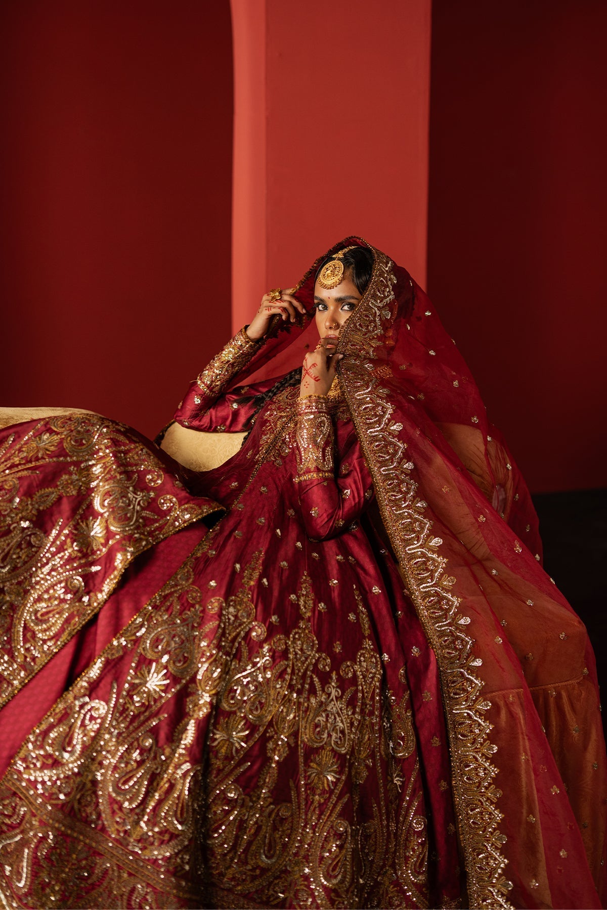 Woman in a traditional red and gold embroidered outfit against a red background